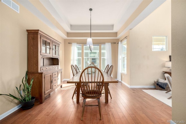 dining space with light wood-type flooring and a tray ceiling