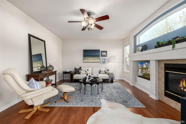 living room featuring a tile fireplace, ceiling fan, and dark wood-type flooring