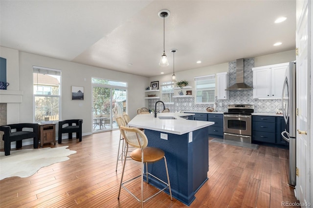 kitchen featuring stainless steel appliances, wall chimney range hood, blue cabinets, white cabinets, and a kitchen breakfast bar