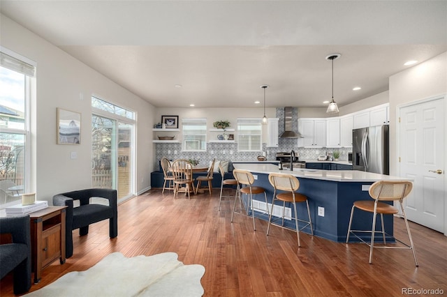 kitchen with stainless steel appliances, wall chimney exhaust hood, a kitchen island with sink, decorative backsplash, and a breakfast bar