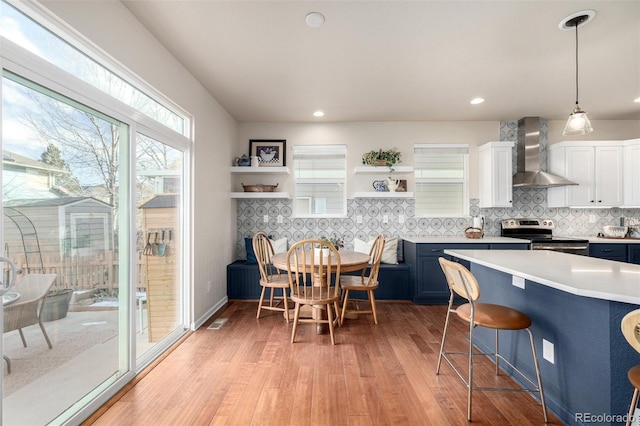 kitchen featuring electric range, a breakfast bar area, hanging light fixtures, wall chimney exhaust hood, and white cabinets