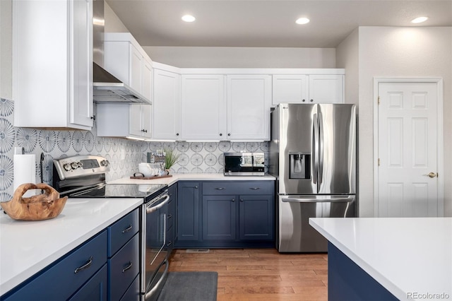 kitchen with white cabinets, wall chimney range hood, blue cabinetry, and appliances with stainless steel finishes