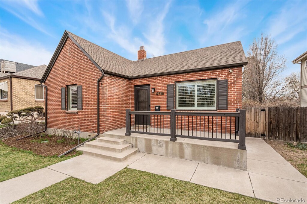 view of front facade with roof with shingles, brick siding, fence, and a chimney
