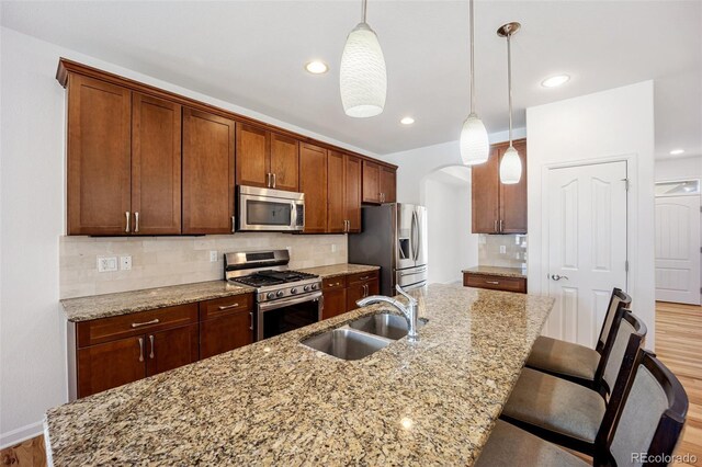 4400 S Ensenada St, Aurora, CO 80015 - kitchen with stainless steel appliances, a sink, arched walkways, a center island with sink, and decorative backsplash