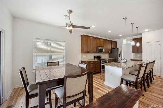 4400 S Ensenada St, Aurora, CO 80015 - kitchen featuring appliances with stainless steel finishes, a sink, light wood-style flooring, tasteful backsplash, and a center island with sink