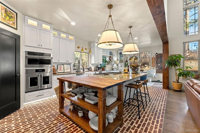 kitchen featuring a kitchen island, wood counters, white cabinetry, and hanging light fixtures