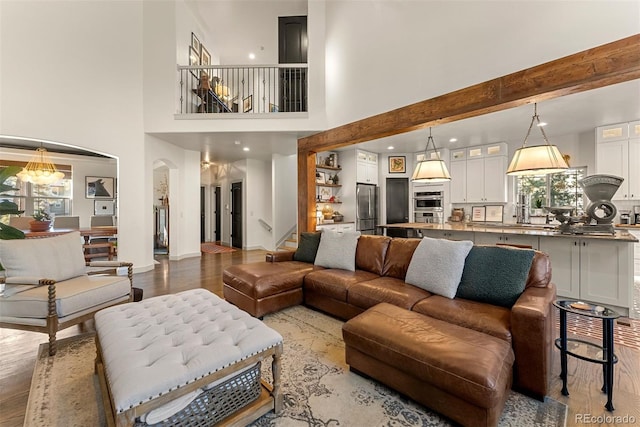 living room featuring beamed ceiling, a towering ceiling, and light wood-type flooring