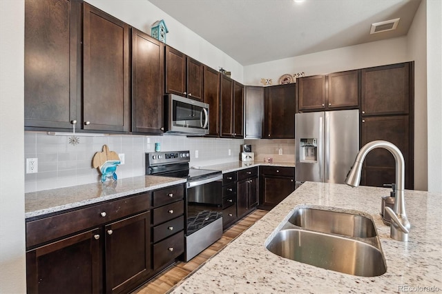 kitchen featuring visible vents, light wood-style flooring, a sink, backsplash, and appliances with stainless steel finishes