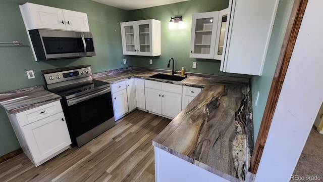 kitchen with sink, white cabinets, kitchen peninsula, appliances with stainless steel finishes, and dark hardwood / wood-style flooring