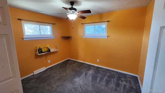 empty room with dark colored carpet, ceiling fan, plenty of natural light, and a textured ceiling