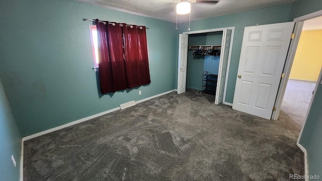 unfurnished bedroom with a textured ceiling, dark colored carpet, ceiling fan, and a closet