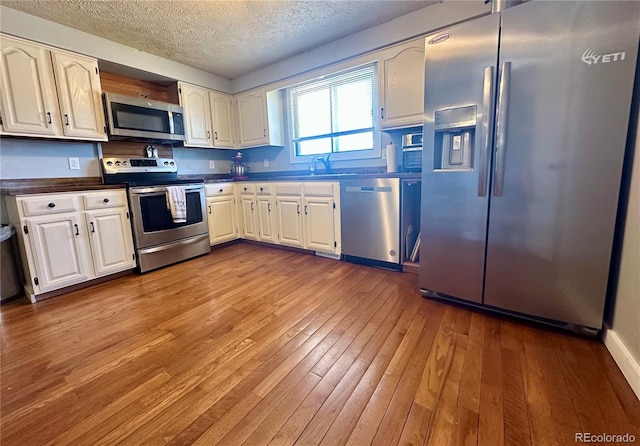 98 Baylor Dr, Buena Vista, CO 81211 - kitchen with appliances with stainless steel finishes, dark countertops, a textured ceiling, light wood-type flooring, and white cabinets