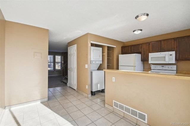 kitchen featuring light tile patterned floors, white appliances, and stacked washer / dryer