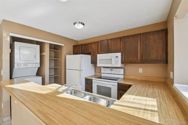 kitchen featuring a textured ceiling, white appliances, stacked washer / drying machine, and sink