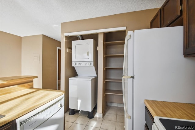 clothes washing area featuring stacked washer / drying machine, light tile patterned flooring, and a textured ceiling