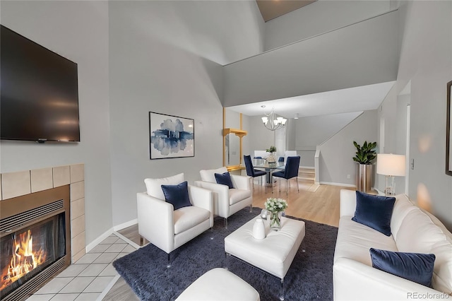 living room with a chandelier, a fireplace, baseboards, light wood-style flooring, and a high ceiling