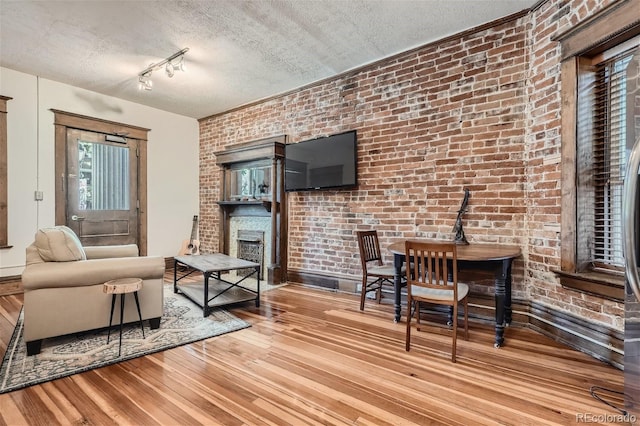 living area featuring a textured ceiling, brick wall, a fireplace, and wood finished floors