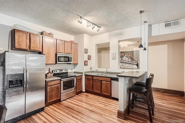 kitchen featuring visible vents, appliances with stainless steel finishes, a peninsula, light wood-type flooring, and a sink