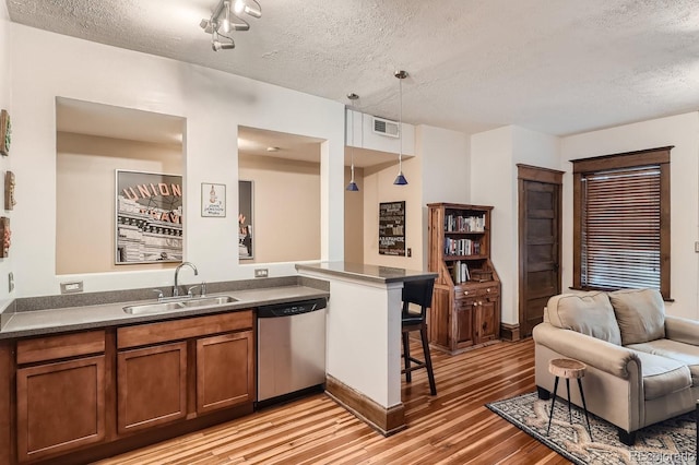 kitchen featuring dishwasher, light wood-style flooring, a breakfast bar, brown cabinets, and a sink