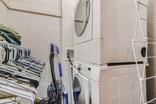 laundry area featuring stacked washer / drying machine and a textured wall