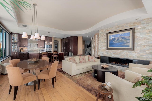 dining area with light hardwood / wood-style floors, a chandelier, a raised ceiling, and a stone fireplace