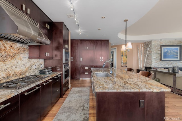 kitchen featuring light wood-type flooring, stainless steel gas cooktop, sink, light stone countertops, and a center island with sink