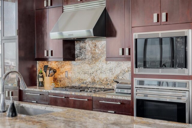 kitchen with exhaust hood, sink, appliances with stainless steel finishes, and light stone countertops