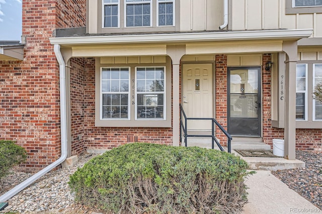 doorway to property featuring board and batten siding, brick siding, and covered porch