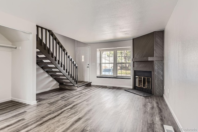 unfurnished living room with wood finished floors, baseboards, stairs, a textured ceiling, and a fireplace