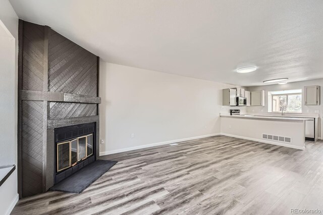 unfurnished living room featuring light wood-type flooring, a fireplace, baseboards, and a sink