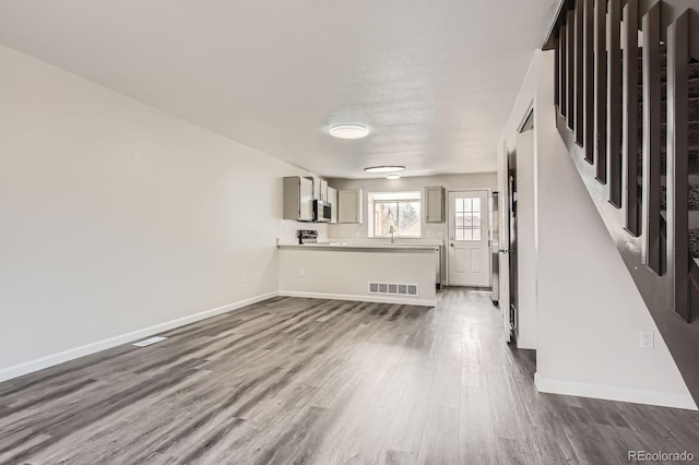 unfurnished living room featuring dark wood-type flooring, baseboards, a sink, and stairway
