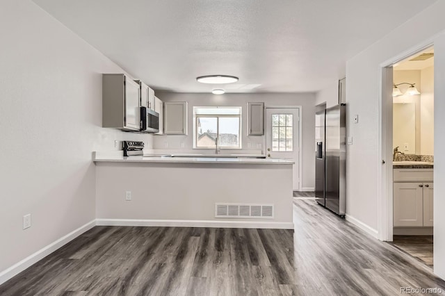 kitchen featuring appliances with stainless steel finishes, a peninsula, dark wood-style flooring, and baseboards
