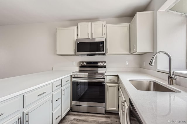 kitchen with appliances with stainless steel finishes, a sink, dark wood finished floors, white cabinetry, and light stone counters