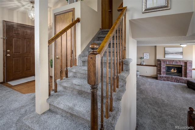 staircase featuring a brick fireplace and carpet