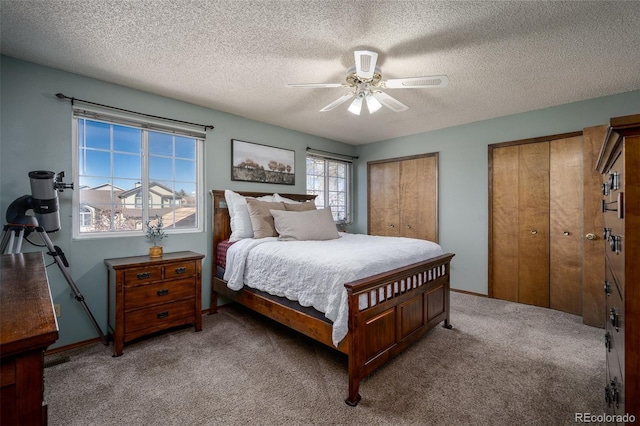 bedroom with light carpet, multiple closets, a ceiling fan, a textured ceiling, and baseboards