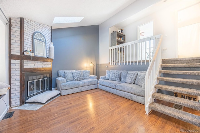 living room featuring lofted ceiling with skylight, hardwood / wood-style floors, and a fireplace