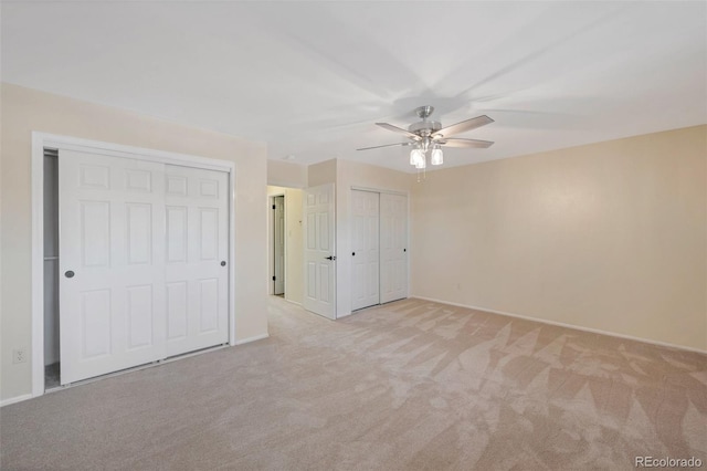 unfurnished bedroom featuring ceiling fan, light carpet, and two closets