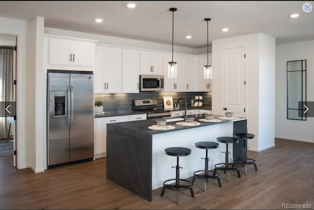 kitchen with pendant lighting, white cabinets, dark wood-type flooring, a center island with sink, and stainless steel appliances