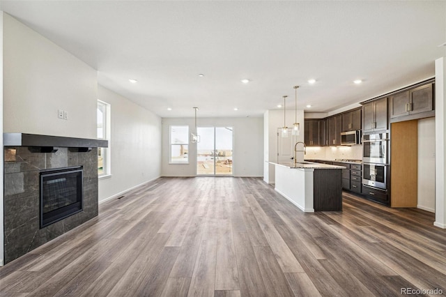 kitchen with a tiled fireplace, dark wood-style floors, appliances with stainless steel finishes, dark brown cabinets, and a sink