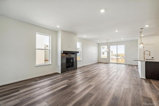 unfurnished living room featuring baseboards, a tile fireplace, dark wood-style floors, a sink, and recessed lighting