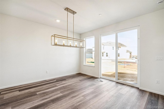 unfurnished dining area featuring a notable chandelier, baseboards, and wood finished floors