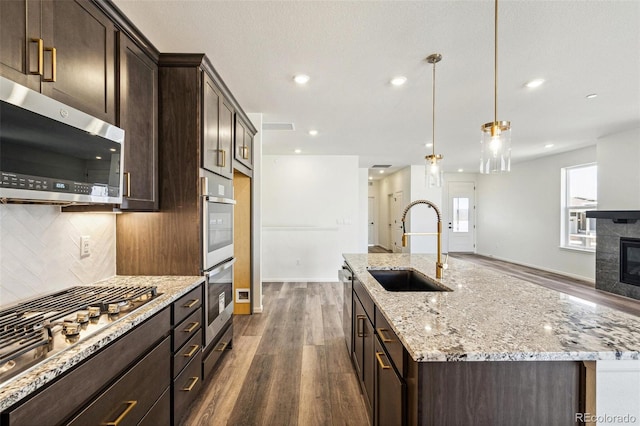 kitchen featuring tasteful backsplash, a center island with sink, a tiled fireplace, appliances with stainless steel finishes, and a sink