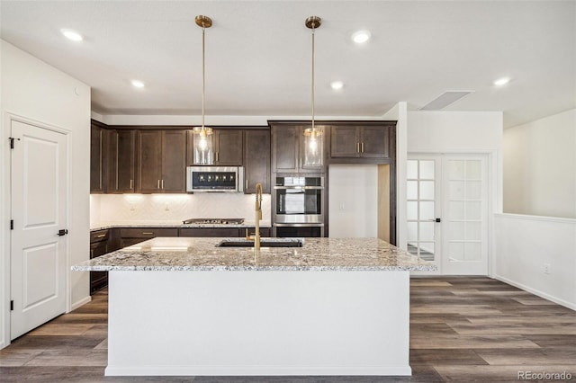 kitchen with stainless steel appliances, dark brown cabinets, dark wood-style flooring, and light stone countertops