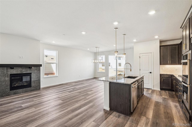 kitchen with appliances with stainless steel finishes, open floor plan, dark brown cabinets, a fireplace, and a sink