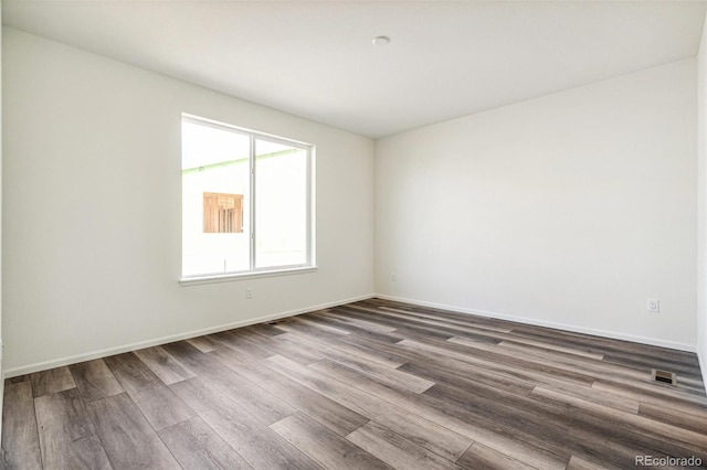 empty room with dark wood-style floors, baseboards, and visible vents