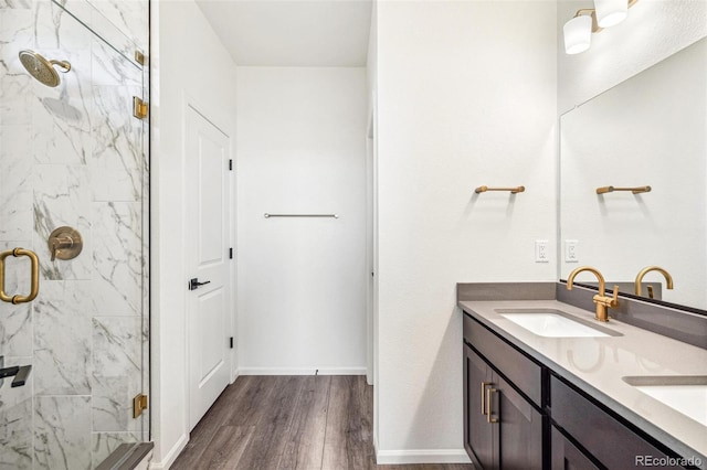 bathroom with a marble finish shower, double vanity, a sink, wood finished floors, and baseboards