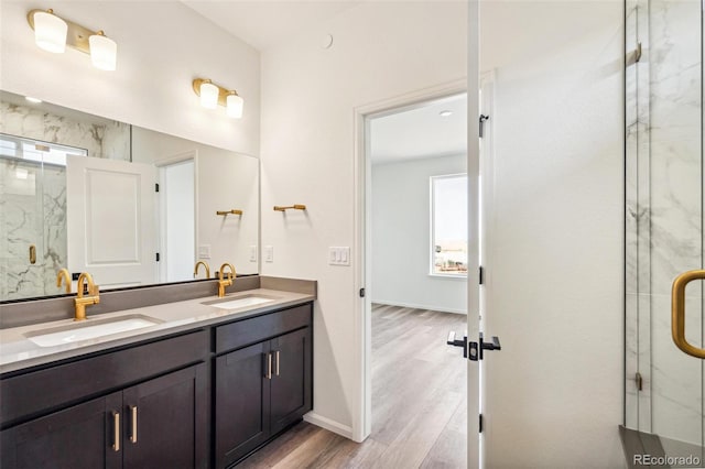 full bathroom featuring double vanity, a marble finish shower, a sink, and wood finished floors