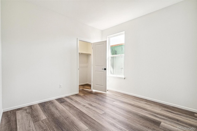 unfurnished bedroom with a closet, wood finished floors, a walk in closet, and baseboards