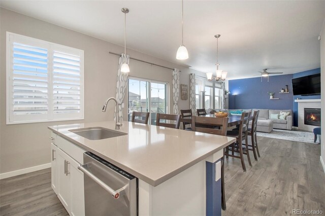 kitchen with dishwasher, a sink, ceiling fan with notable chandelier, a glass covered fireplace, and light wood-style flooring