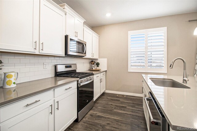 kitchen featuring backsplash, appliances with stainless steel finishes, dark wood finished floors, a sink, and baseboards